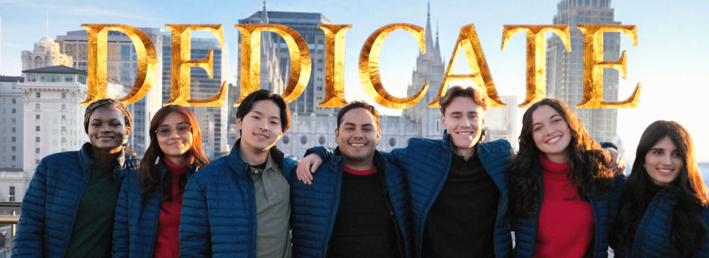 A-group-of-seven-young-adults-smile-at-the-camera-in-front-of-a-cityscape-with-the-word-DEDICATE-superimposed